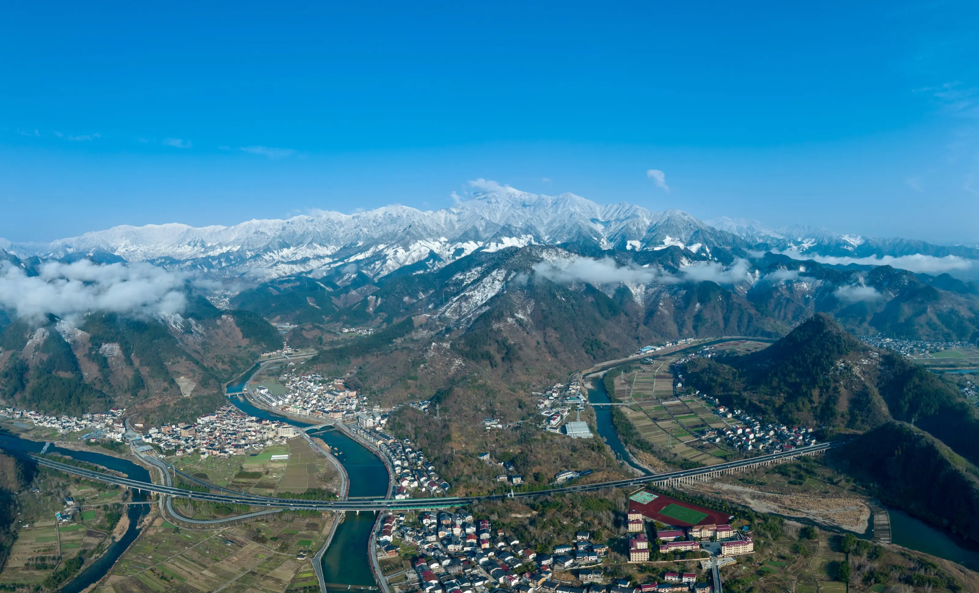 Aerial panorama of a river valley beneath snow mountains
