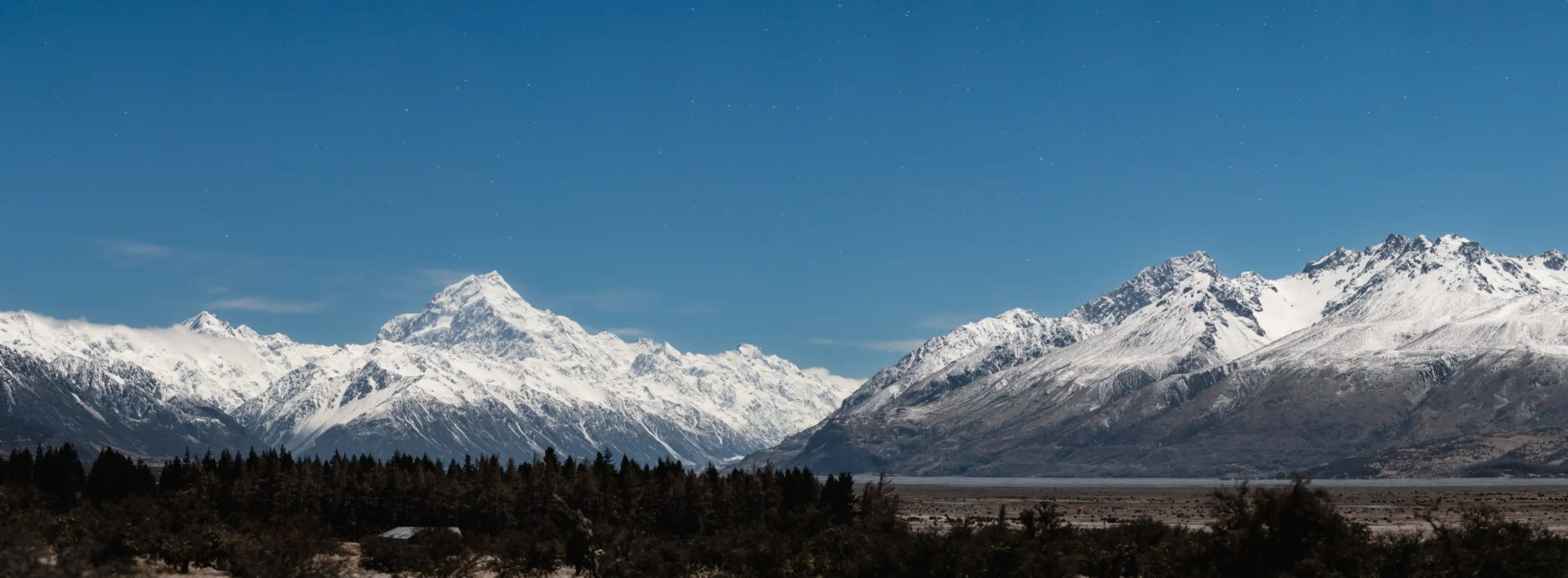A snowline panorama of alpine peaks above dark forest